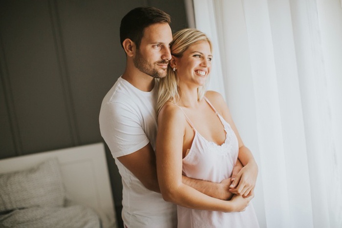 Lovely young couple standing by the window at morning
