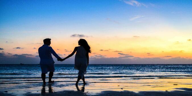 A couple holding hands walking on the beach at sunrise